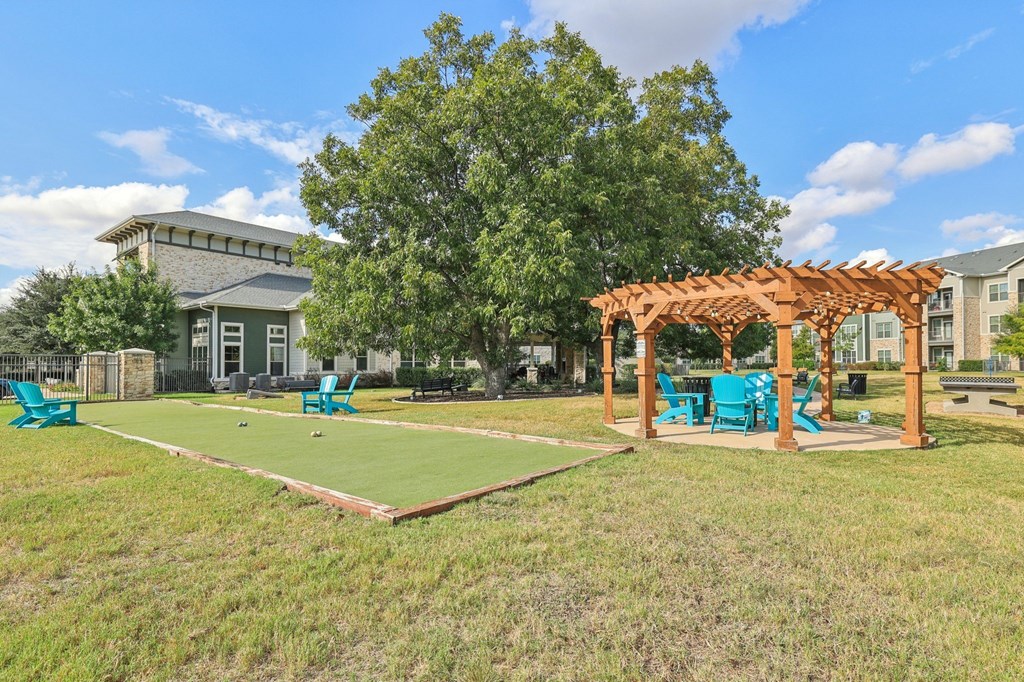 A sunny day at the park with a shuffleboard court and a pergola.