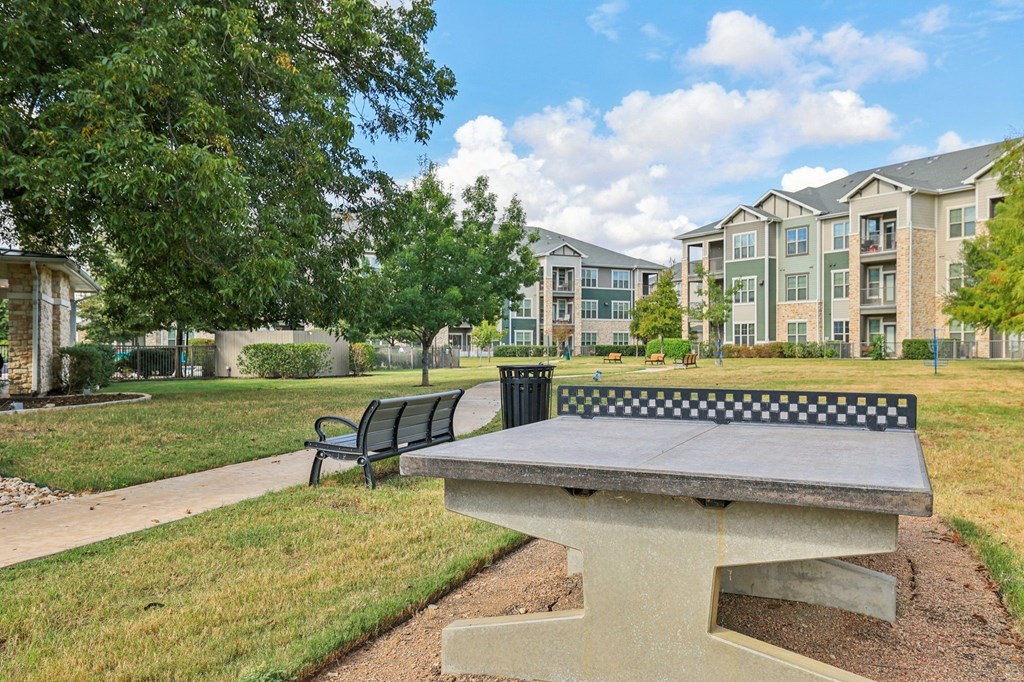 A concrete bench with a black and white checkered back sits in a grassy area.
