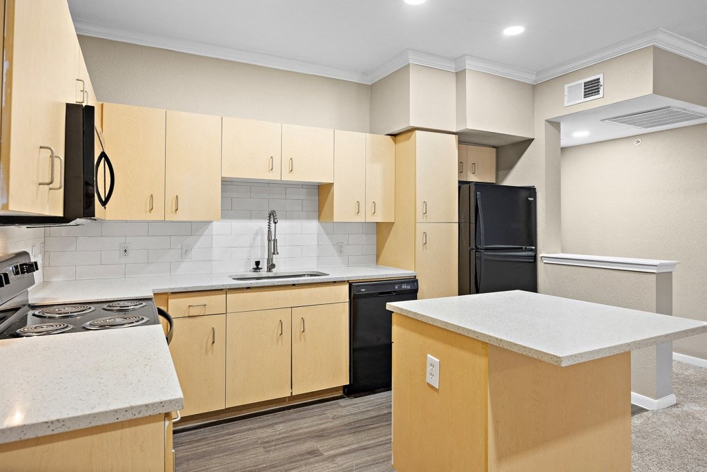 a kitchen with white countertops and wooden cabinets with black appliances at Artisan Apartments & Shops