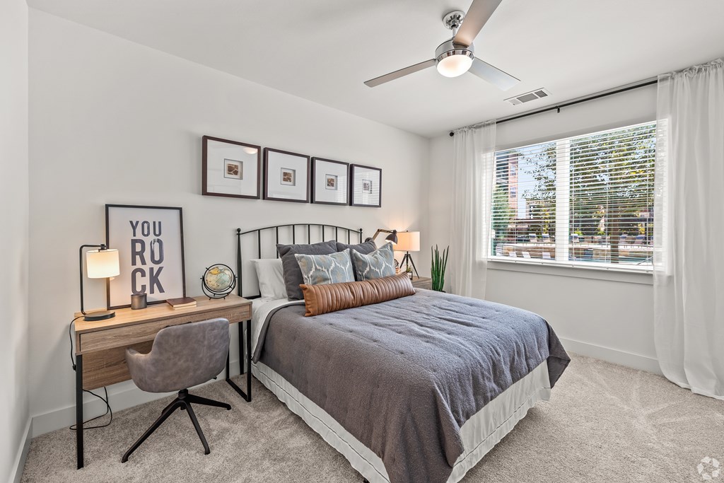 A bedroom with a bed, desk, chair, and pictures on the wall.