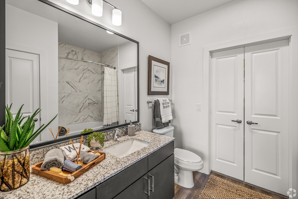 A bathroom with a marble countertop and a wooden tray with toiletries on it. at Aurora Watson Branch, Mansfield, TX