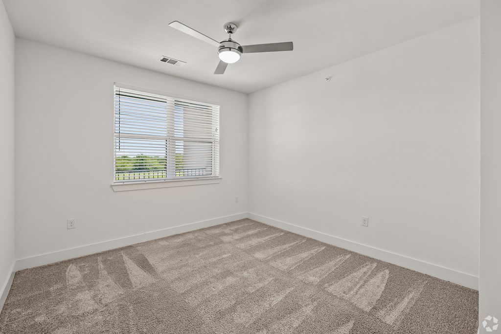 A room with a fan, carpet, and a window.