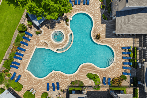 A large blue swimming pool surrounded by a brick patio and lounge chairs.