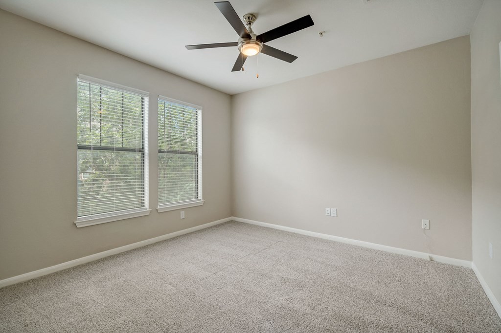 an empty living room with a ceiling fan and two windows