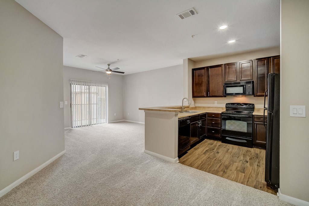 an empty living room with a kitchen with a stove and refrigerator