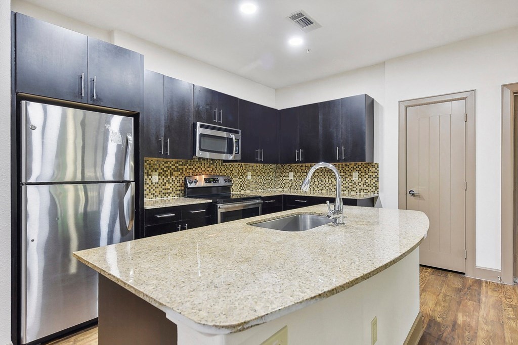 a kitchen with black cabinets and a granite counter top and a stainless steel refrigerator at Lakeline East Apartments, Cedar Park