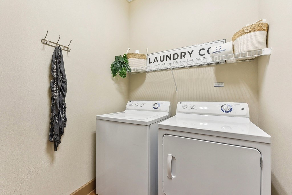 a washer and dryer in a laundry room with a shelf on the wall at Lakeline East Apartments, Cedar Park, TX