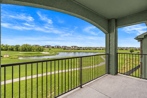 A balcony overlooks a green field and a body of water.