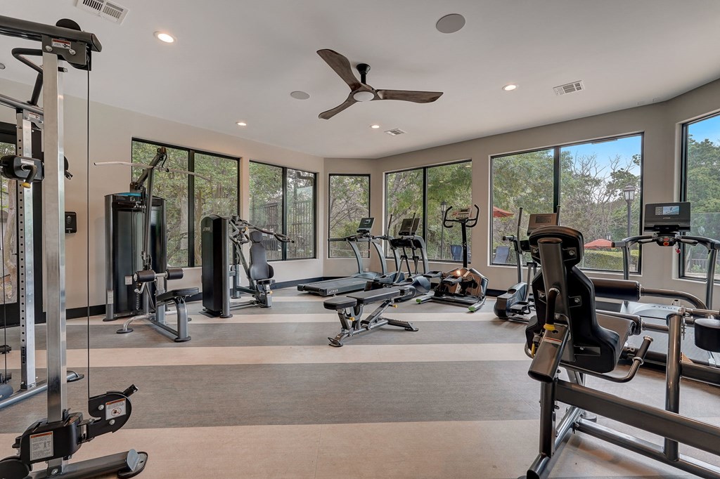 a gym with cardio equipment and windows in a home with a view of the woods at Legends on the Green Apartments, San Antonio 78232