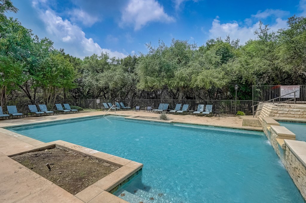 a swimming pool with chairs around it and trees in the background