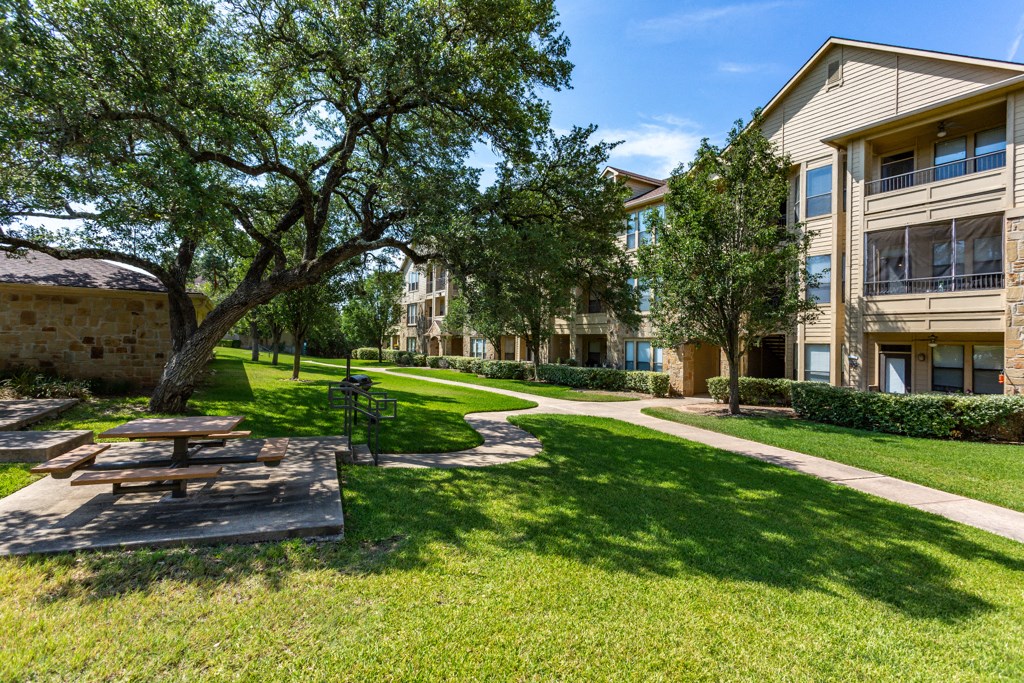 a picnic area with a table and benches in front of an apartment building at The Verandah, Austin, TX, 78726