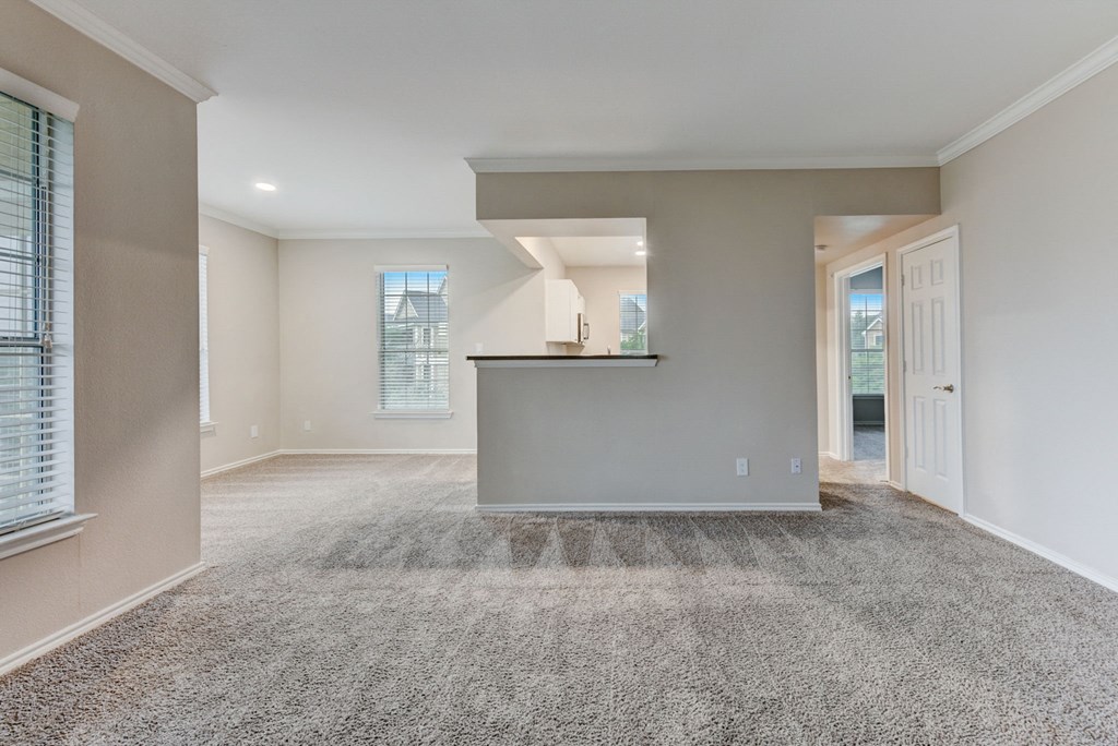 an empty living room with carpet and a kitchen