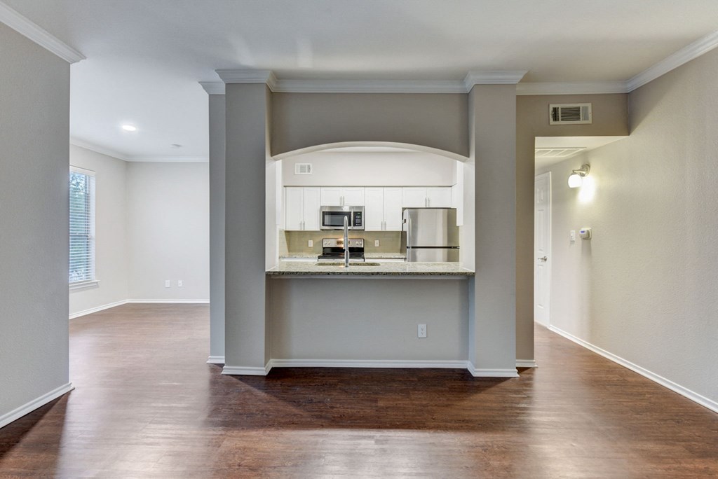 an empty living room and kitchen with a hard wood floor