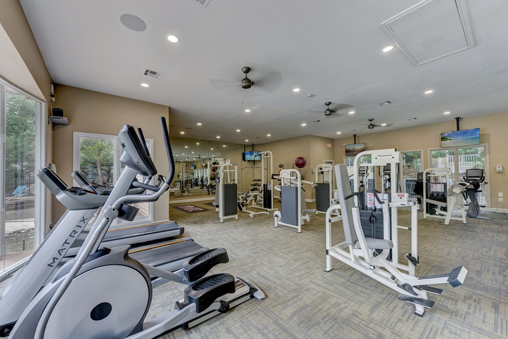 a gym with cardio equipment and weights in a building with windows