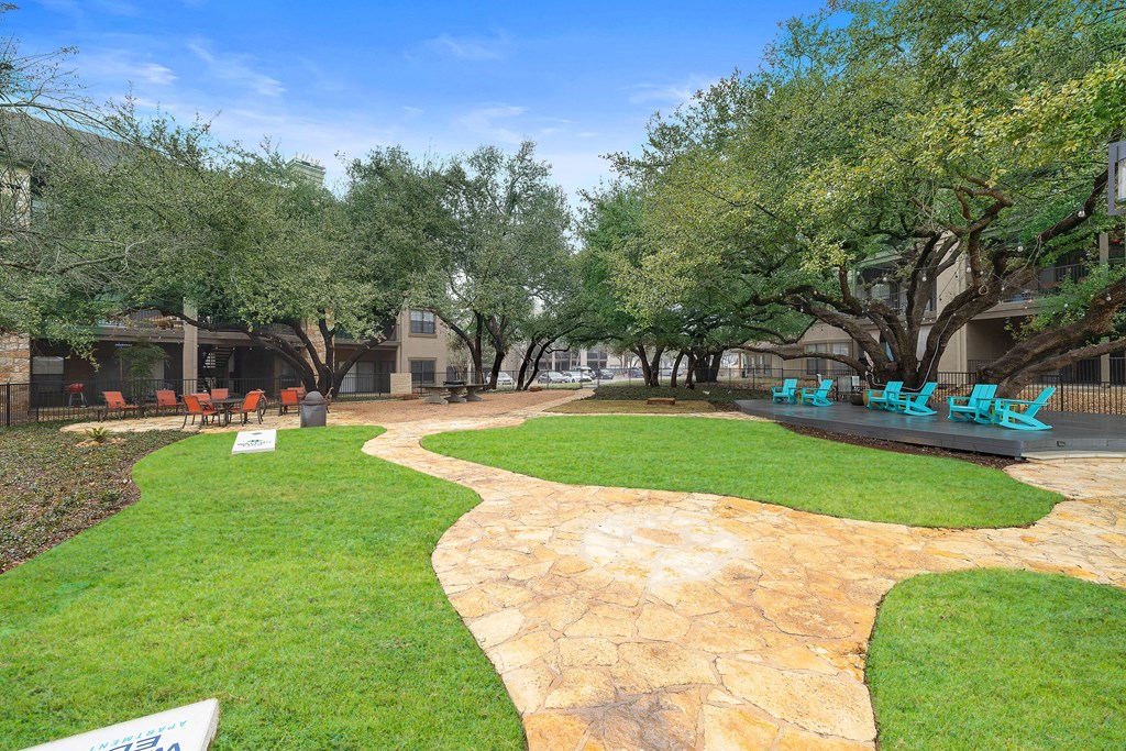 a park with grass and trees and a patio with blue chairs at Waters Edge Apartment Homes, Texas
