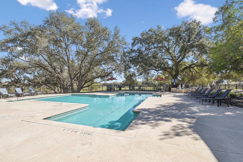 a swimming pool with chairs around it and trees at TalaVera Apartments, San Antonio 78232