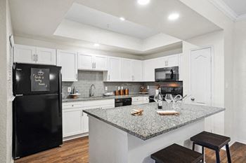 A black fridge in a kitchen with white cabinets at La Ventura Apartments, Texas, 75093