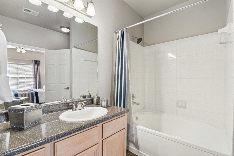a bathroom with a sink and a tub and a mirror at Legends on the Green Apartments, San Antonio, Texas