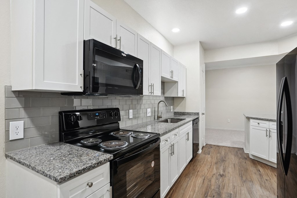 a kitchen with white cabinets and black appliances and a black microwave at La Ventura Apartments, Plano, 75093