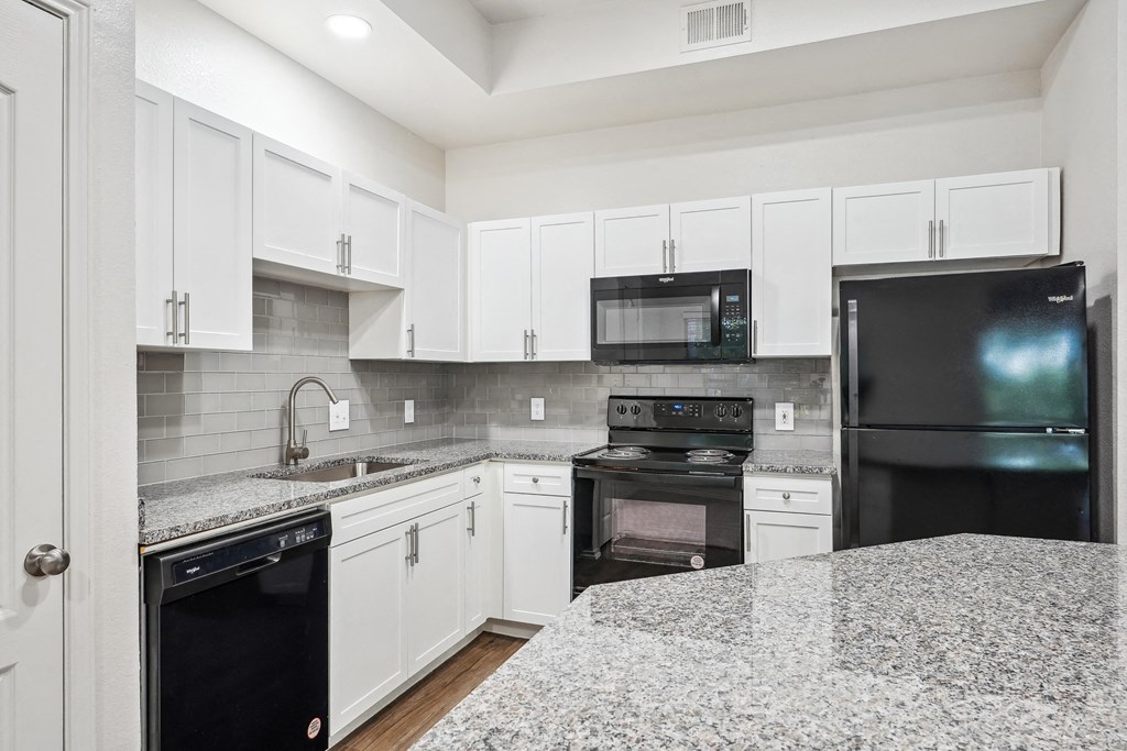 a kitchen with granite counter tops and black appliances at La Ventura Apartments, Texas, 75093