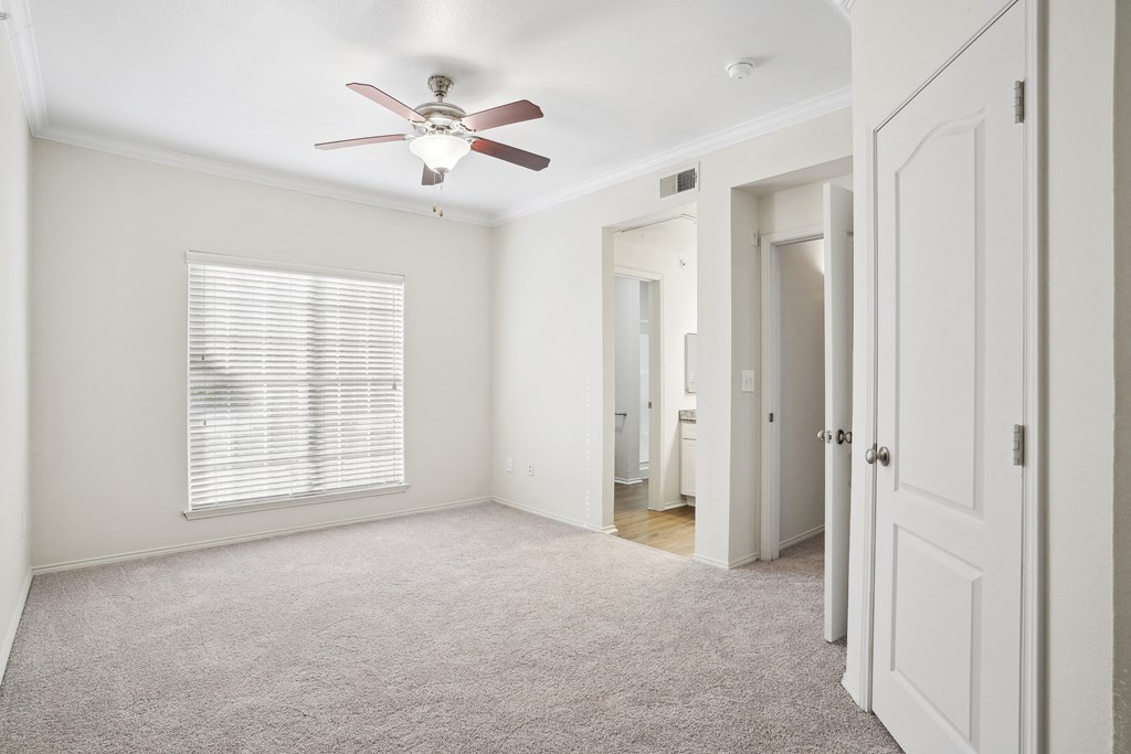 an empty bedroom with a ceiling fan and a door to a bathroom at La Ventura Apartments, Texas