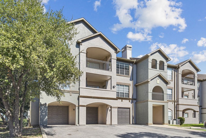 an apartment building with two garages and a tree at Legends on the Green Apartments, San Antonio 78232