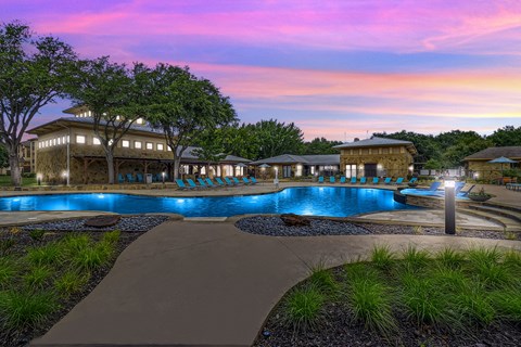 Illuminated resort pool at twilight with stone buildings at The Canyons Apartments, Fort Worth