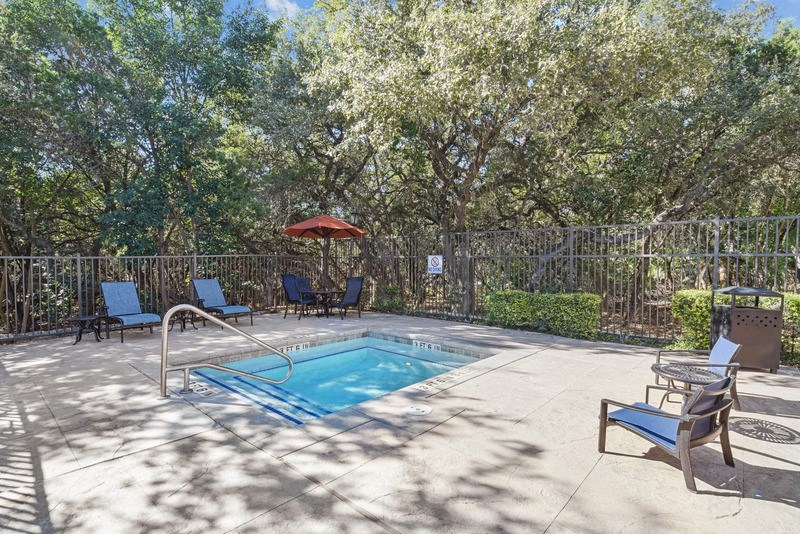 a pool with chairs and an umbrella in a backyard with trees at Legends on the Green Apartments, San Antonio