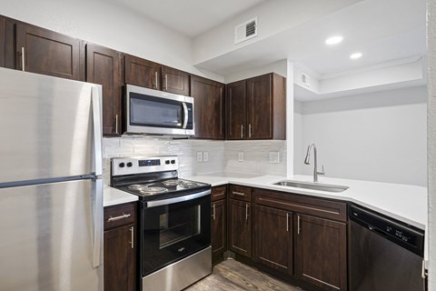 a kitchen with dark wood cabinets and stainless steel appliances at The Legends at Eagle Mountain Lake, Fort Worth, Texas