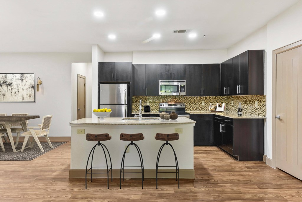 a kitchen with black cabinets and a counter with three stools at Lakeline East Apartments, Cedar Park, TX