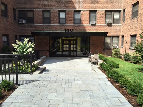 The image shows the entrance to a brick building with a black gate and a stone pathway leading to the door.