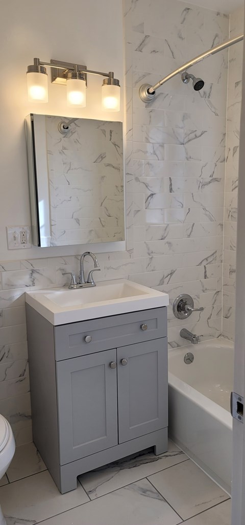 A bathroom with a sink, mirror, and grey cabinet.