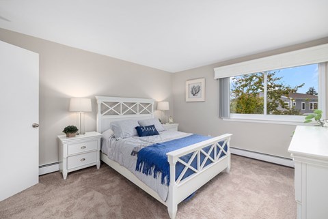 A bedroom with a white bed and a window with a view of a house.