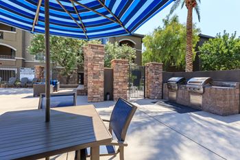 a patio with a table and chairs and a blue and white umbrella at The Preserve by Picerne, N Las Vegas, 89086