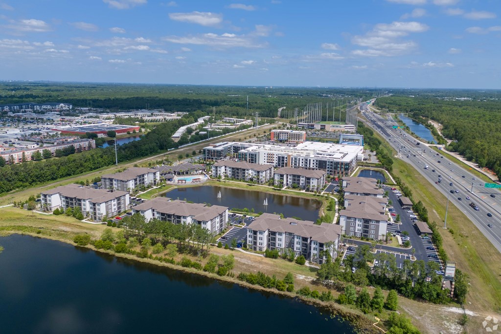 A bird's eye view of a residential complex with a lake in the foreground and a highway in the background.
