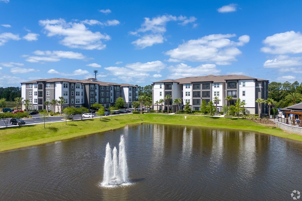 A fountain in the middle of a pond in front of apartment buildings.