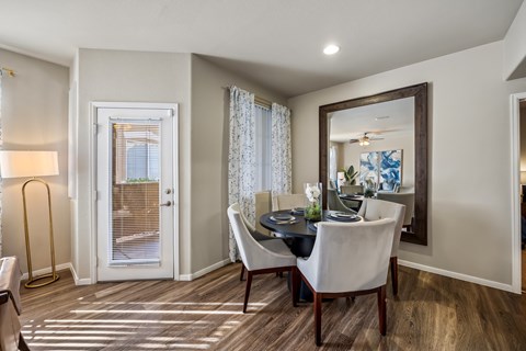 A dining room with a table set for two and a view of a door with blinds.