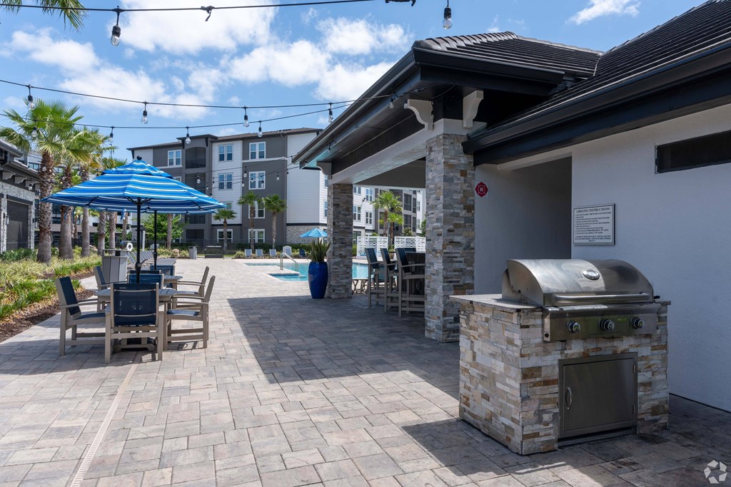 A patio with a grill and chairs under a blue umbrella.