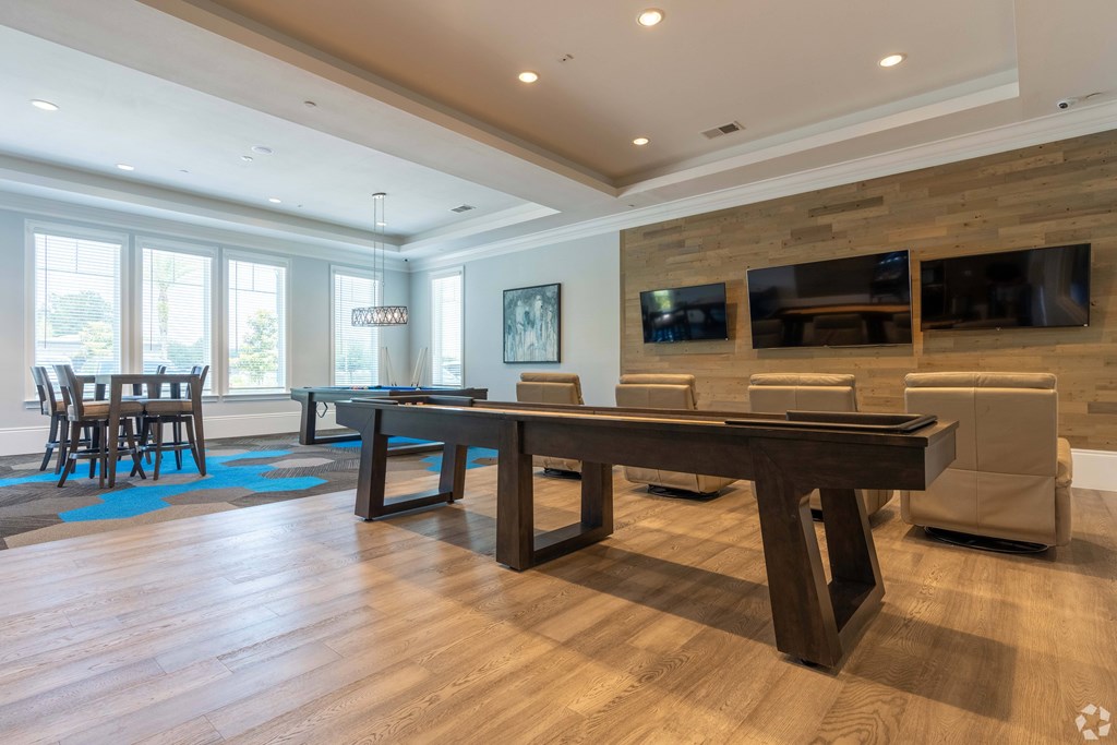 A large wooden table is in the middle of a room with a blue rug and chairs.