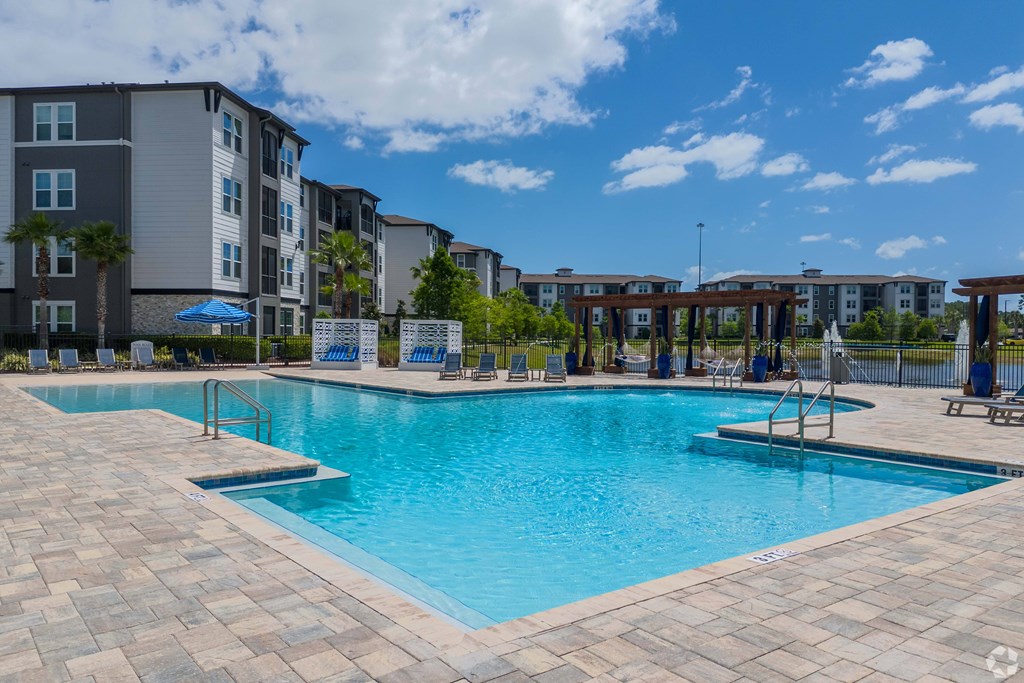 A large swimming pool surrounded by a brick patio and apartment buildings.