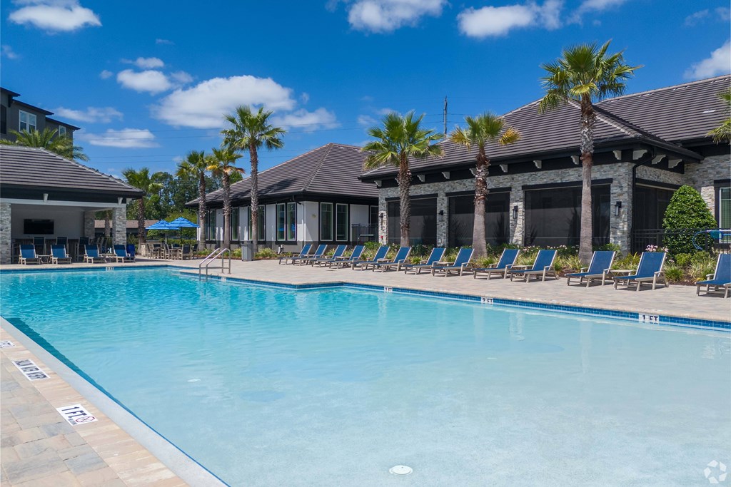 A large swimming pool with lounge chairs and palm trees in front of a house.