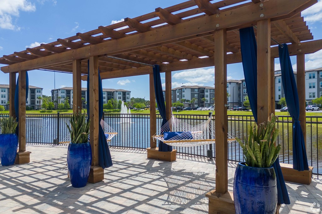 A wooden pergola with blue vases and plants is in the foreground with apartment buildings in the background.