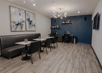 A modern dining area with a grey booth, a white table, and a painting on the wall.