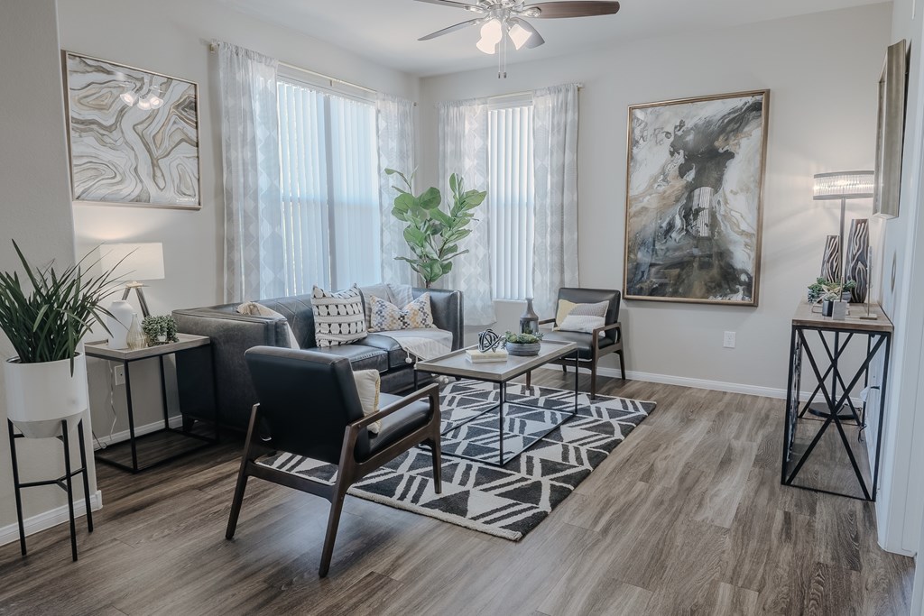 A living room with a black and white rug, a black leather couch, a wooden chair, a white side table, a potted plant, and a painting on the wall.