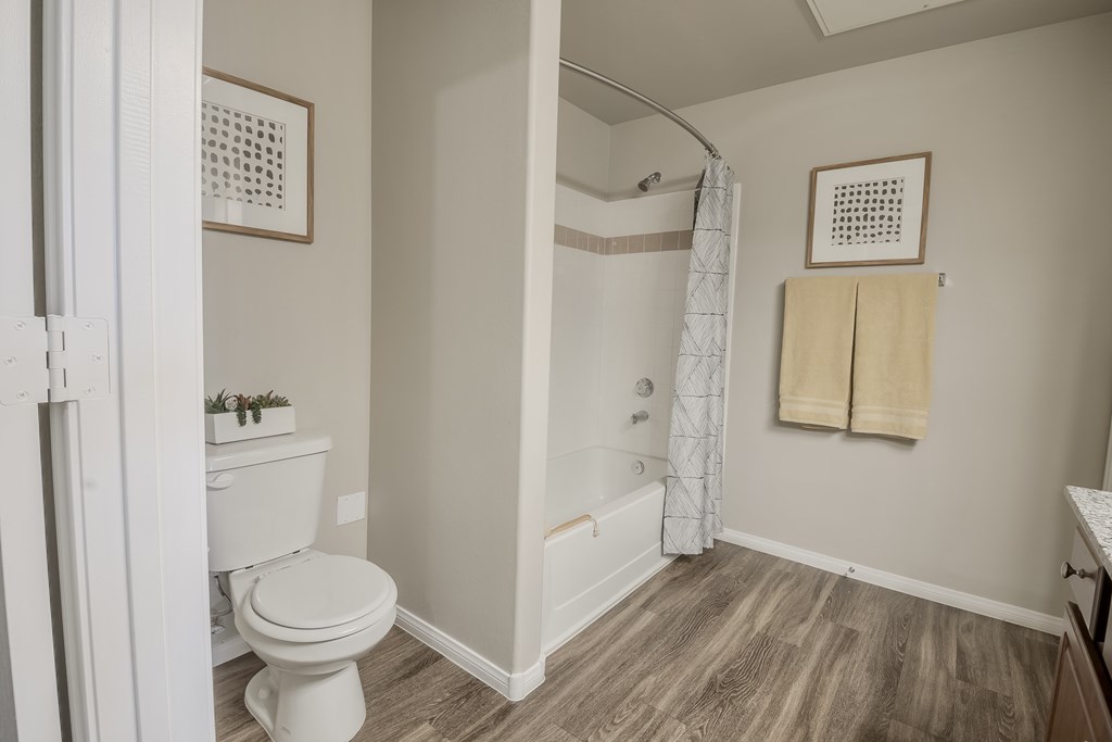 A small bathroom with a toilet, a bathtub, and a wooden floor.