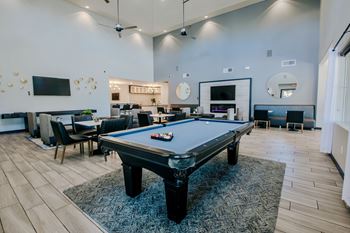A pool table is in the middle of a room with a TV and a bar.