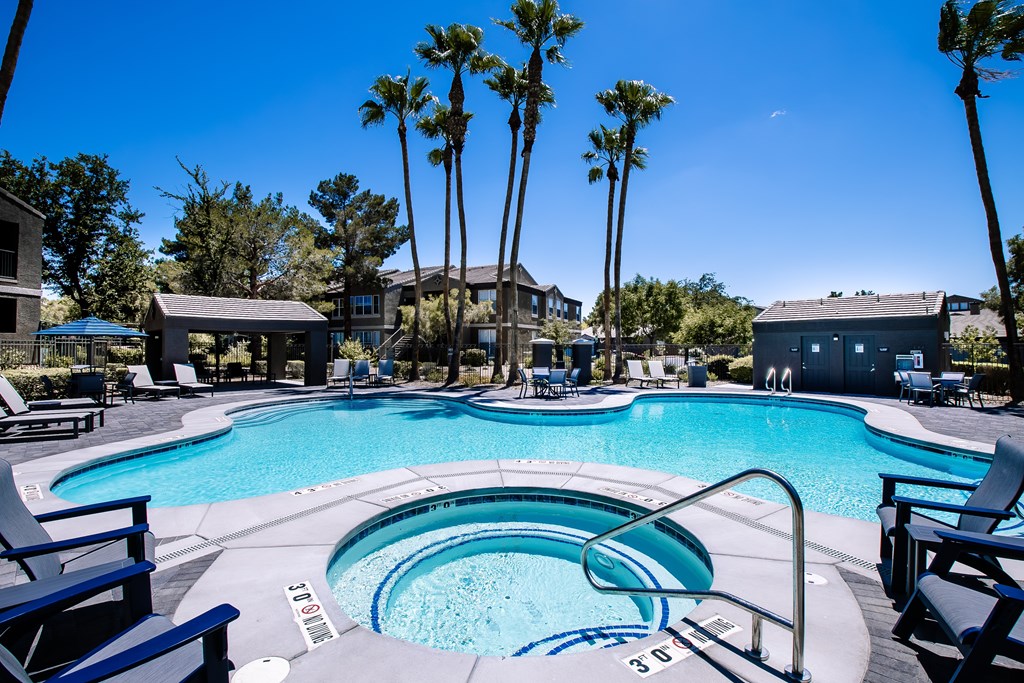 Large swimming pool and spa surrounded by Palm Trees and chairs.