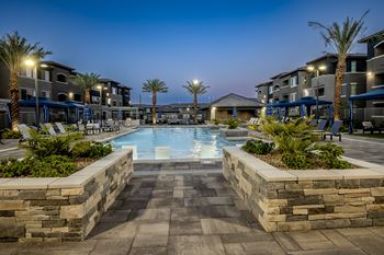 Night shot of the beautiful resort-style pool surrounded by palm trees and cabanas at Level 25 at The Curve by Picerne, Las Vegas, NV