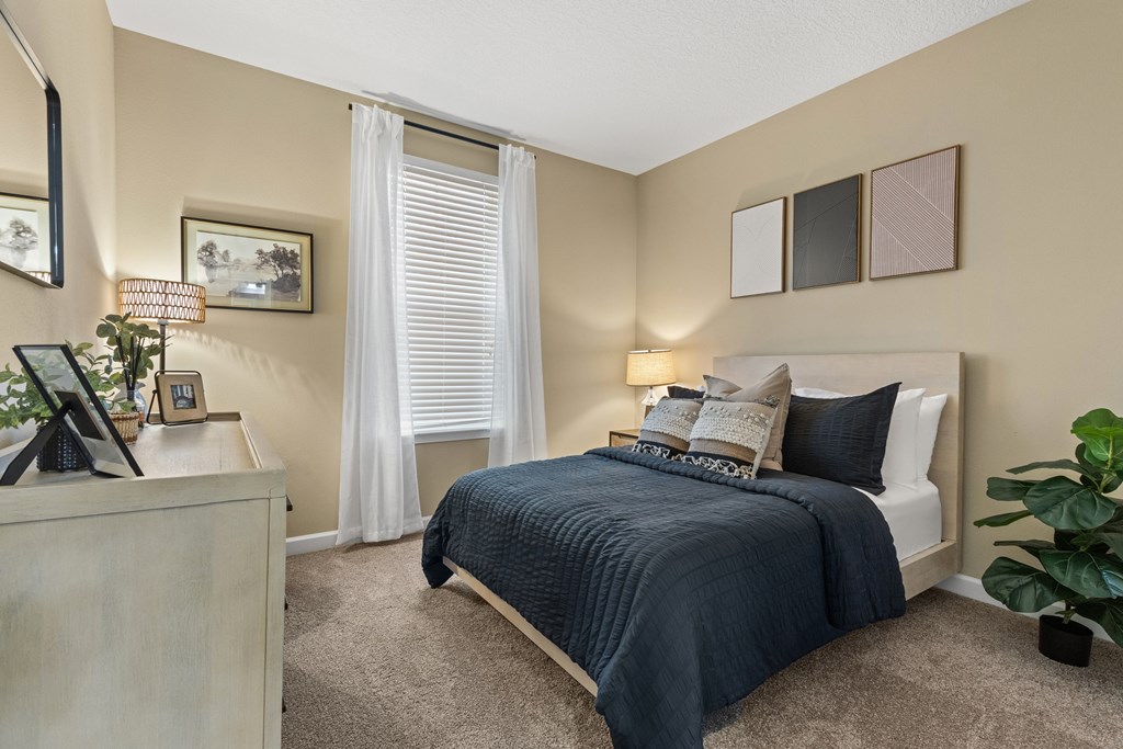 A bedroom with a bed, nightstand, and a plant.