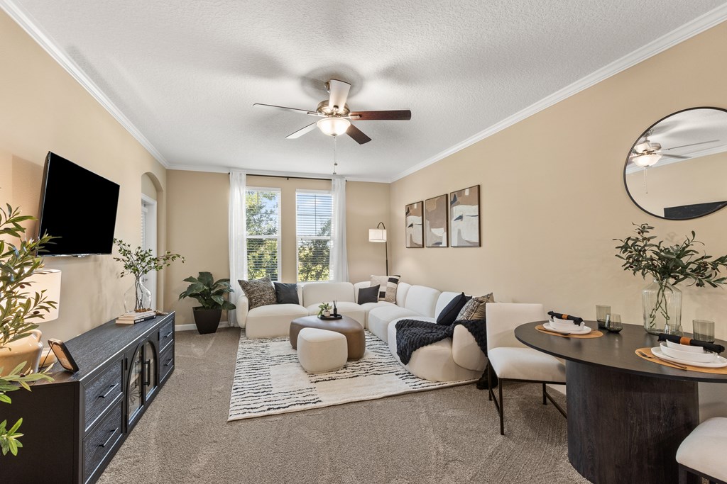 A living room with a ceiling fan and a flat screen TV mounted on the wall.